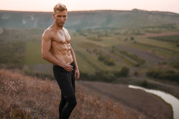 Спортсмен без рубашки позирует на холме — стоковое фото