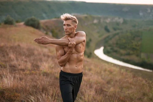 Sportovní košili muž strečink svalů na přírodu — Stock fotografie
