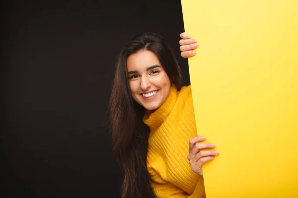 Cheerful woman hiding behind yellow banner — Stock Photo, Image