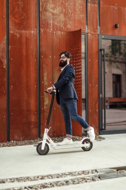 Sakallı adam sokakta scooter kullanıyor.