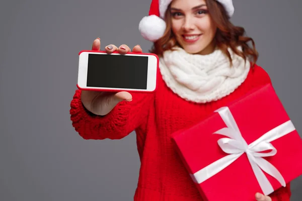 Весела жінка з різдвяним подарунком, що показує смартфон — стокове фото