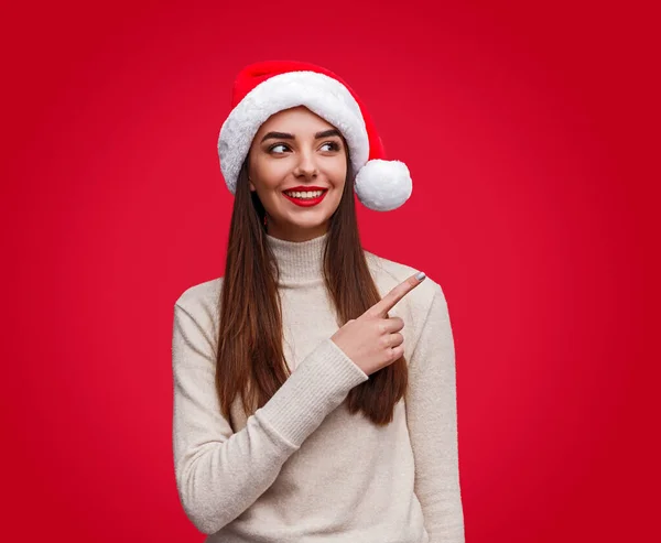 Allegro giovane donna in cappello di Natale punta sopra la spalla — Foto Stock