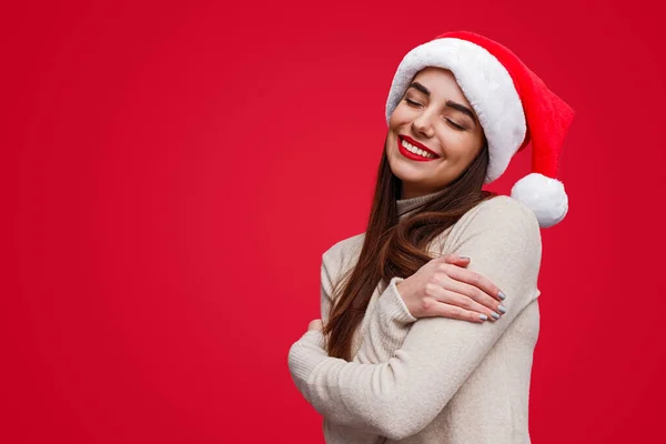 Charmante dromerige vrouw in Santa hoed omarmen armen armen — Stockfoto