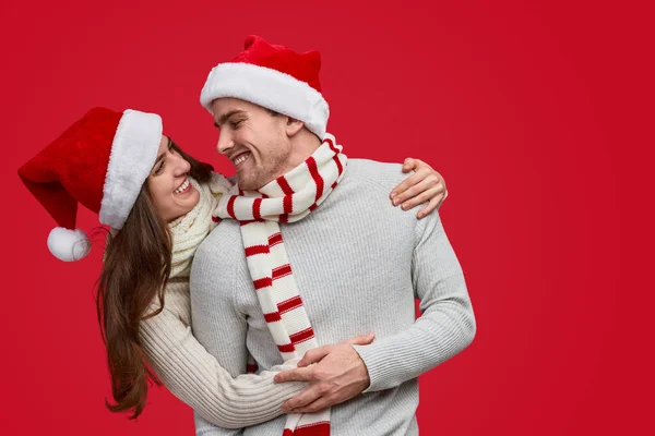 Радісна пара в червоному різдвяному капелюсі і шарф обіймає і посміхається — стокове фото