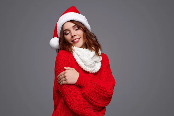 Mulher macia em chapéu de Santa e suéter abraçando braços — Fotografia de Stock