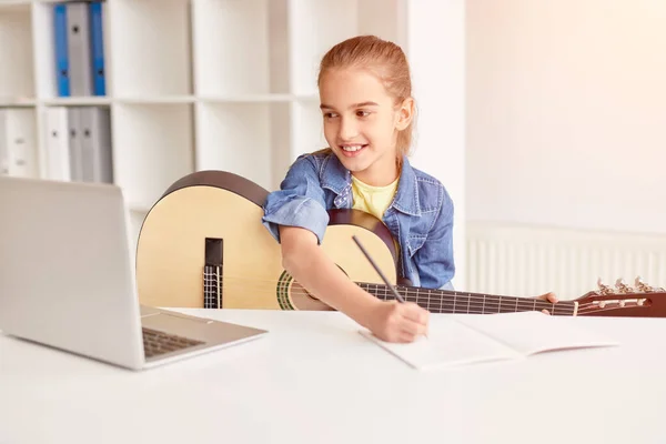Весела дитина робить нотатки під час онлайн-гітарного уроку — стокове фото