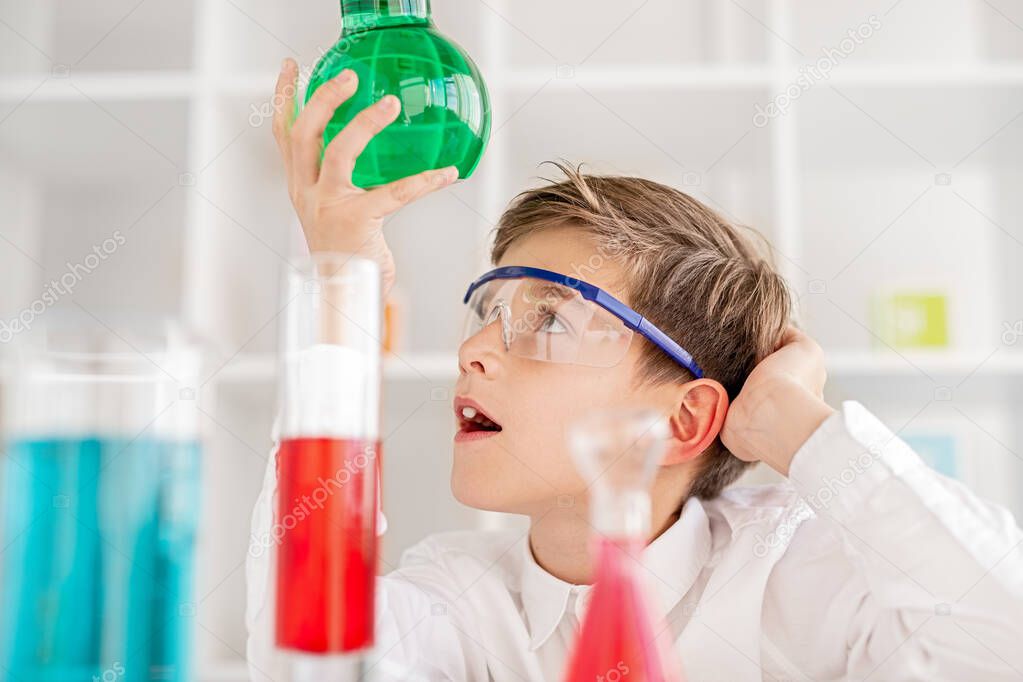 Puzzled boy examining chemical substance in flask