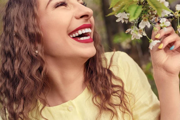 Сміється жінка насолоджується квітами на дереві в саду — стокове фото