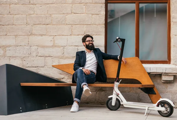 Hipster relajante cerca de scooter eléctrico en el banco —  Fotos de Stock