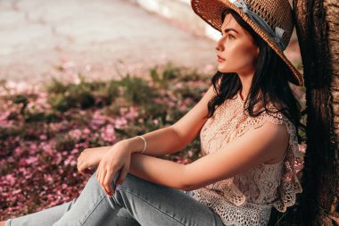 Sakin bir kadın ağaçların altında oturmuş, rüya gibi gözlerini kaçırıyor.