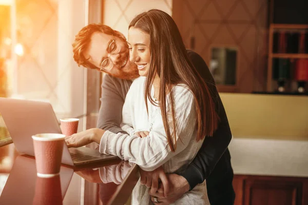 Smiling man hugging woman working on laptop at table — Stock Photo, Image
