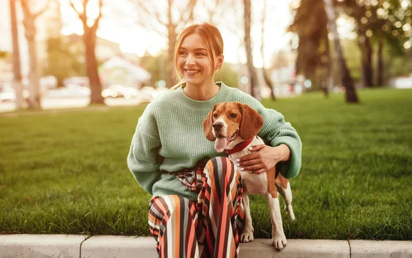 Mujer sonriente vinculación perro adorable y sentado en la hierba — Foto de Stock