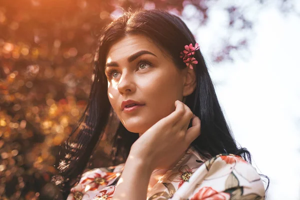 Zufriedene Frau mit Blume hinter dem Ohr berührt Gesicht im warmen Sonnenlicht — Stockfoto