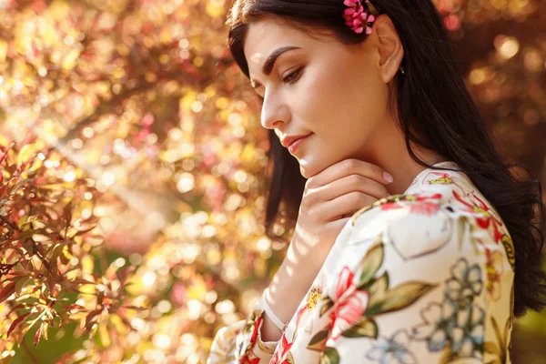 Mulher pensativa com flor atrás da orelha na luz solar quente — Fotografia de Stock