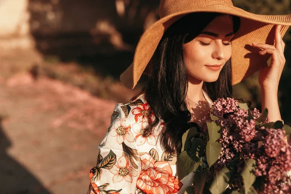 Mulher encantadora segurando chapéu de sol e andando com olhos de fechamento de buquê — Fotografia de Stock