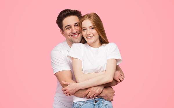 Delighted couple hugging and looking at camera