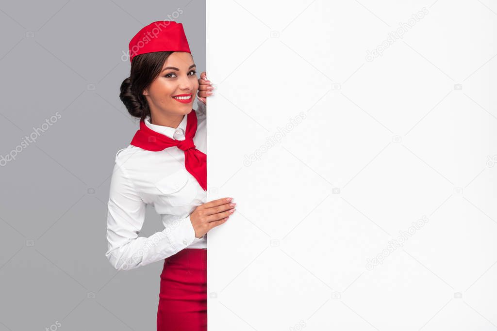 Cheerful air hostess peeking out from behind blank banner