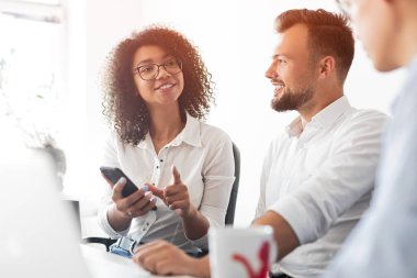 Akıllı telefonlu neşeli siyahi kadın meslektaşlarıyla konuşuyor.