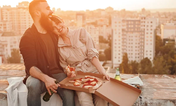 Casal feliz beber cerveja e comer pizza no telhado — Fotografia de Stock