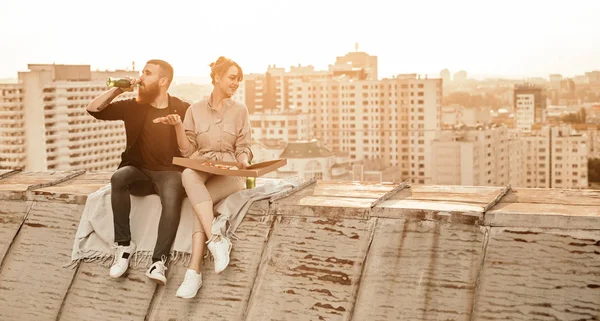 Pareja joven disfrutando de pizza y cerveza en la azotea — Foto de Stock