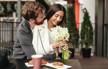 Amorous Kafe 'nin dışında çiçeklerle büyüleyici bir kadına sarılıyor.