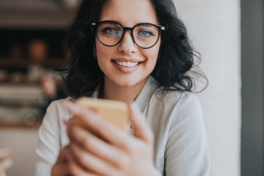 Kafede akıllı telefon kullanan neşeli genç bir kadın.