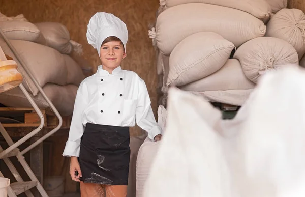 Pequeño panadero alegre cerca de bolsas de harina —  Fotos de Stock