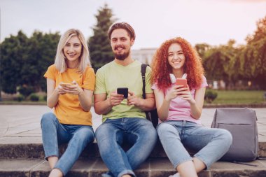 Parkta akıllı telefon kullanan neşeli öğrenciler