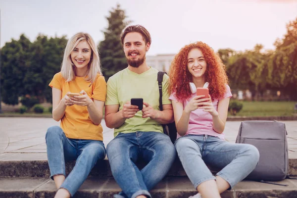 Estudantes alegres usando smartphones no parque — Fotografia de Stock