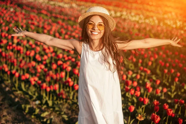 Glückliche Frau, die Hände auf dem Tulpenfeld ausbreitet und in die Kamera blickt — Stockfoto