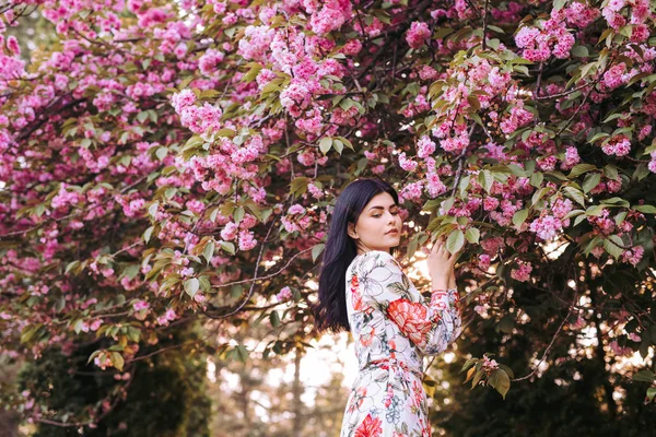 ผู้หญิงอ่อนโยนที่น่าสนใจ ยืนอยู่ข้างต้นไม้ดอกไม้สีชมพูในสวน — ภาพถ่ายสต็อก