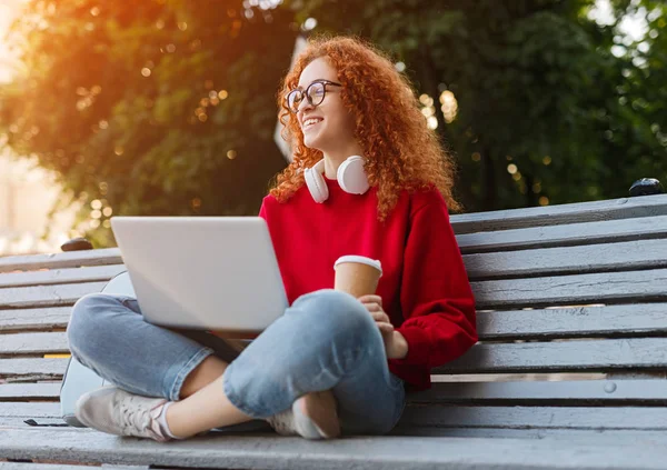 Happy woman with laptop and coffee sitting on bench — Stock Photo, Image