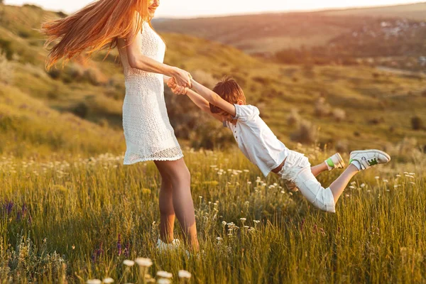 Teen girl spinning little brother on meadow — Stock Photo, Image