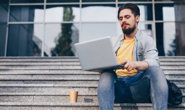 Genç adam basamaklarda dizüstü bilgisayar kullanıyor