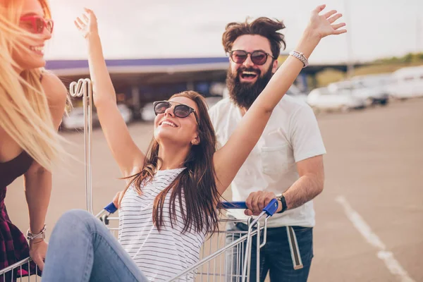 Vrolijke hipster duwen winkelwagentje met vrienden — Stockfoto