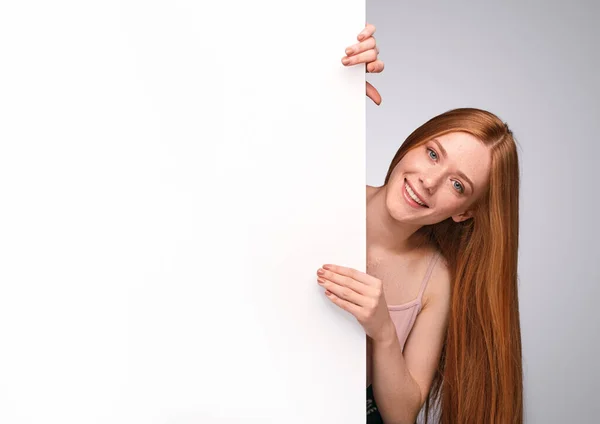 Cheerful ginger woman peeking out from empty placard — 스톡 사진