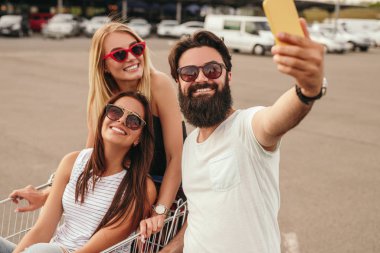 Delighted modern friends taking selfie during shopping