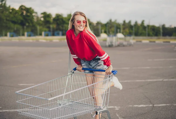 Joyful woman with shopping cart standing on parking Royalty Free Stock Images