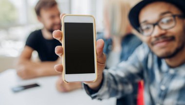 Young man sitting in cafe and showing smartphone