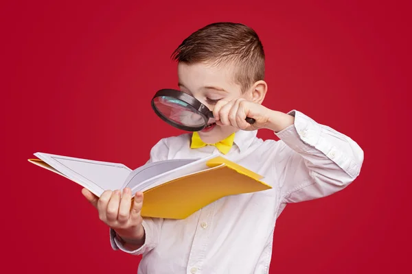 Inquisitive boy reading book through magnifying glass — Stockfoto