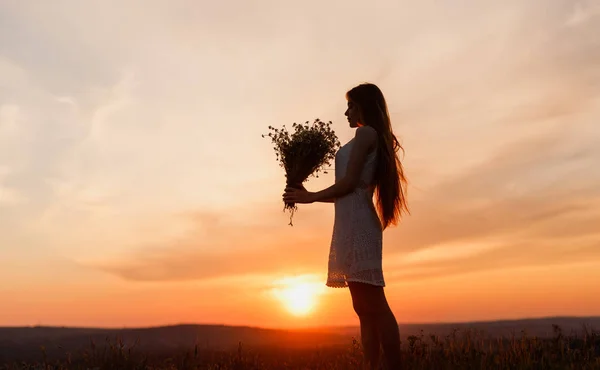 Woman with wildflowers standing on field at sunset — Stock Photo, Image