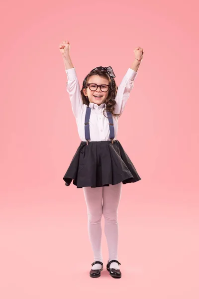 Pequeña colegiala emocionada con las manos levantadas sobre fondo rosa — Foto de Stock