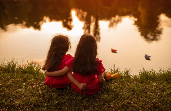 Meninas irreconhecíveis sentadas na margem do lago à noite — Fotografia de Stock