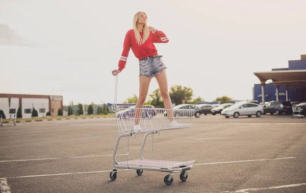 Stylová žena stojící na nákupním vozíku na parkovišti — Stock fotografie