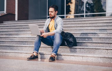 Merdivenlerde oturan ve dizüstü bilgisayar kullanarak genç adam