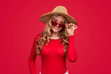 Şapkalı ve güneş gözlüklü mutlu bir kadın kameraya bakıyor.