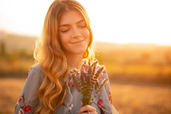 Mutlu genç kadın gün batımında çiçek kokusu alıyor. — Stok fotoğraf
