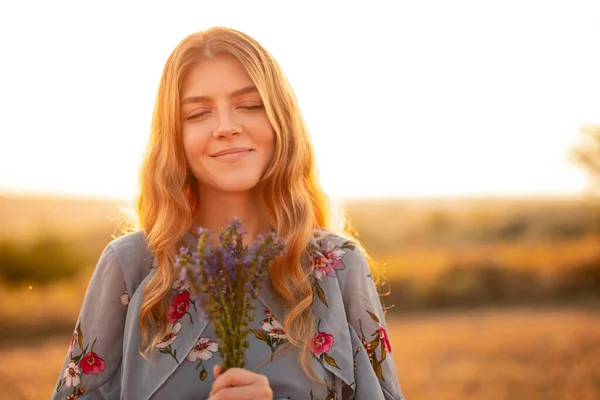Ευτυχισμένη νεαρή γυναίκα με λουλούδια στον αγρό — Φωτογραφία Αρχείου