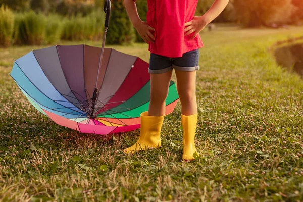 Confident kid in rain boots standing near umbrella