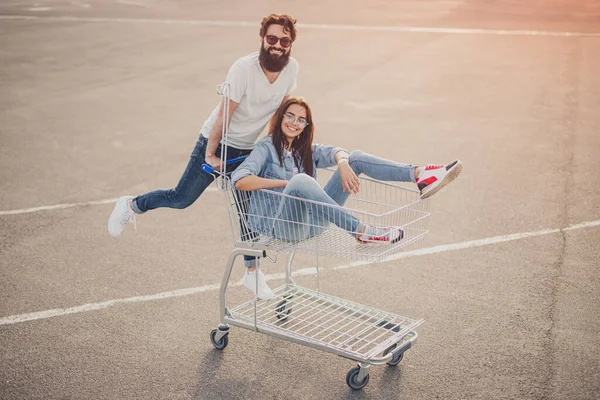 Cheerful couple riding shopping cart on parking — 图库照片